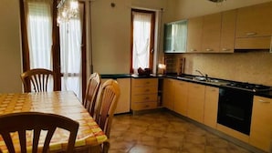 A dining area with a checkered table and chairs, a kitchen with wooden cabinets and a stove, and a chandelier. - Casa Granseola (Alghero)