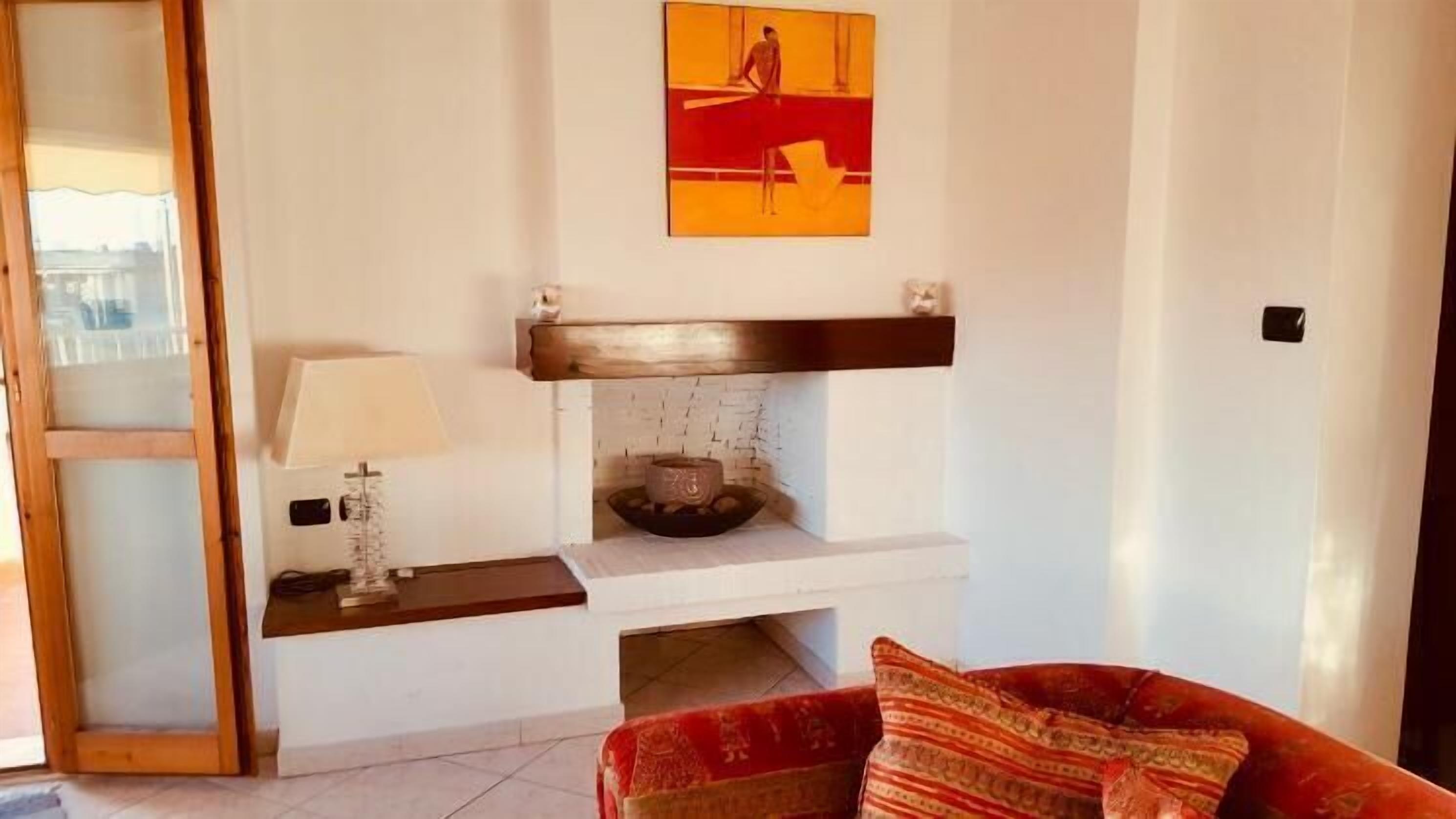 A living room with a fireplace, a red sofa, a lamp, and a painting on the wall.