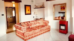 A living room with a patterned sofa, a red heater, a mirror, and a framed picture on the wall. - Casa Granseola (Alghero)