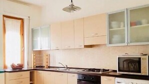 A kitchen with light-colored cabinets, a microwave, an oven, and a washing machine. - Casa Granseola (Alghero)