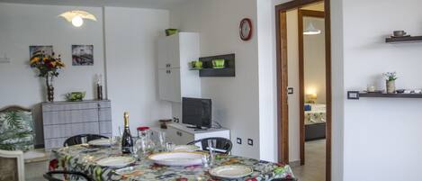 Un comedor con una mesa dispuesta para cuatro personas, un televisor y un reloj en la pared.
