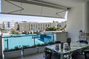 Un balcon avec vue sur la piscine, un espace salon extérieur et une vue sur la ville en arrière-plan.