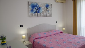 Un dormitorio con cama, lámparas de noche, aire acondicionado instalado en la pared y un cuadro de flores.
