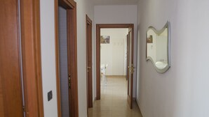 Un pasillo con puertas de madera, suelo de baldosas y un espejo en la pared derecha.