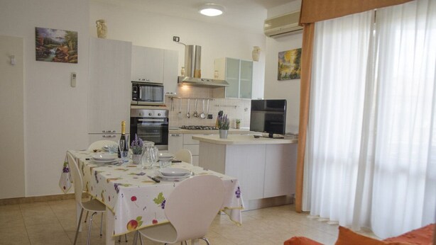 Una cocina moderna con armarios blancos, una mesa de comedor con platos y cubiertos, y un televisor sobre la encimera.