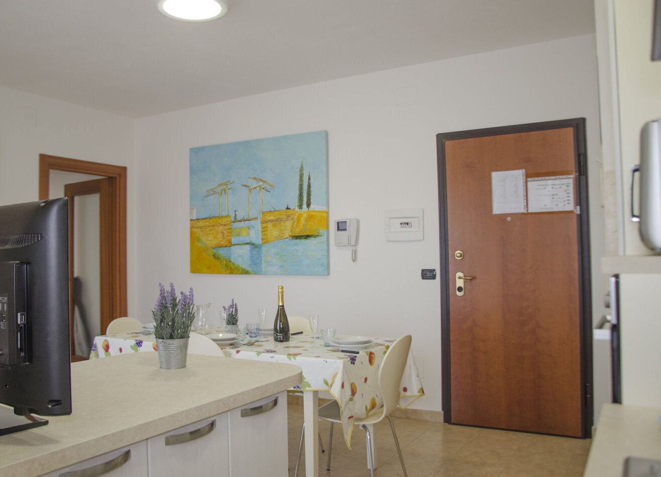 Une pièce avec une table à manger dressée pour deux personnes, un téléviseur sur le côté gauche et une porte avec un tableau d’affichage sur le côté droit.