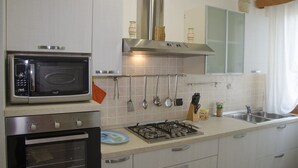 Una cocina equipada con microondas, horno, cocina a gas, utensilios colgantes y un lavabo.