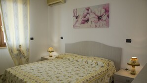 Un dormitorio con colcha estampada, dos mesitas de noche con lámparas, un cuadro en la pared y una ventana con cortinas.