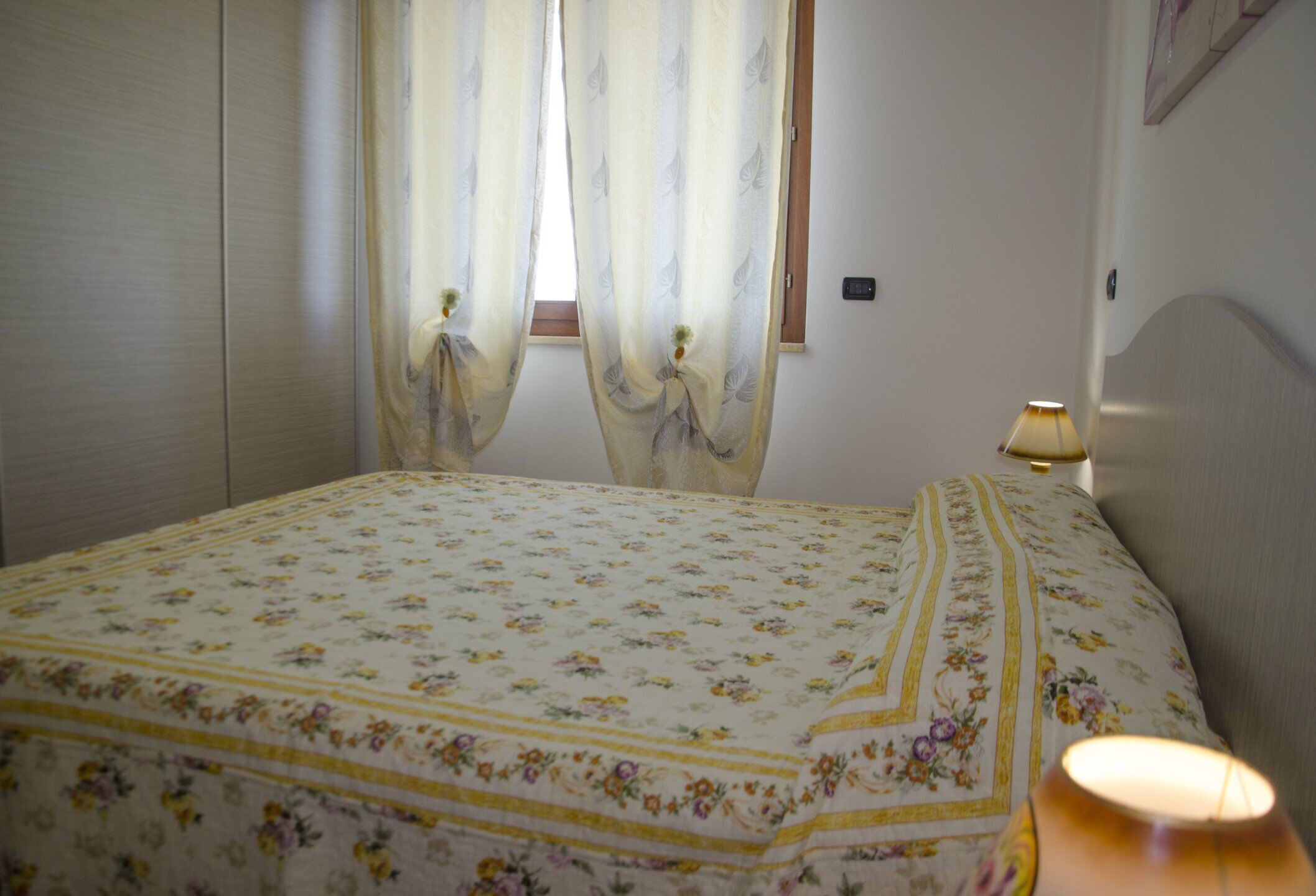A bedroom with a floral bedspread, a bedside lamp, and curtains.