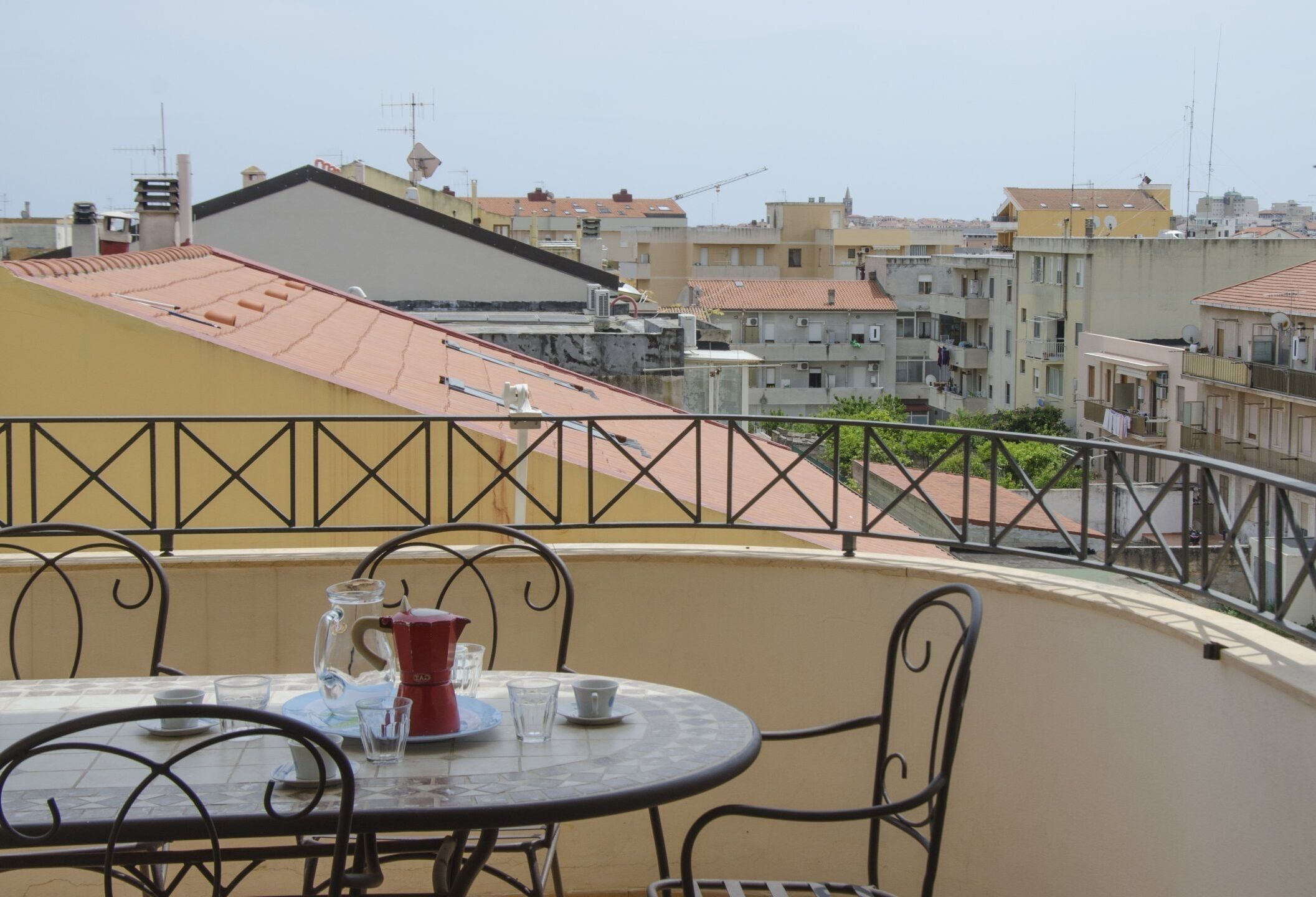 A balcony with a table and chairs, a pitcher, and glasses.