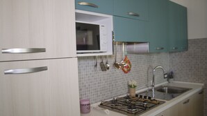 Ett kök med vita skåp, en mikrovågsugn, en gasspis och ett handfat.
