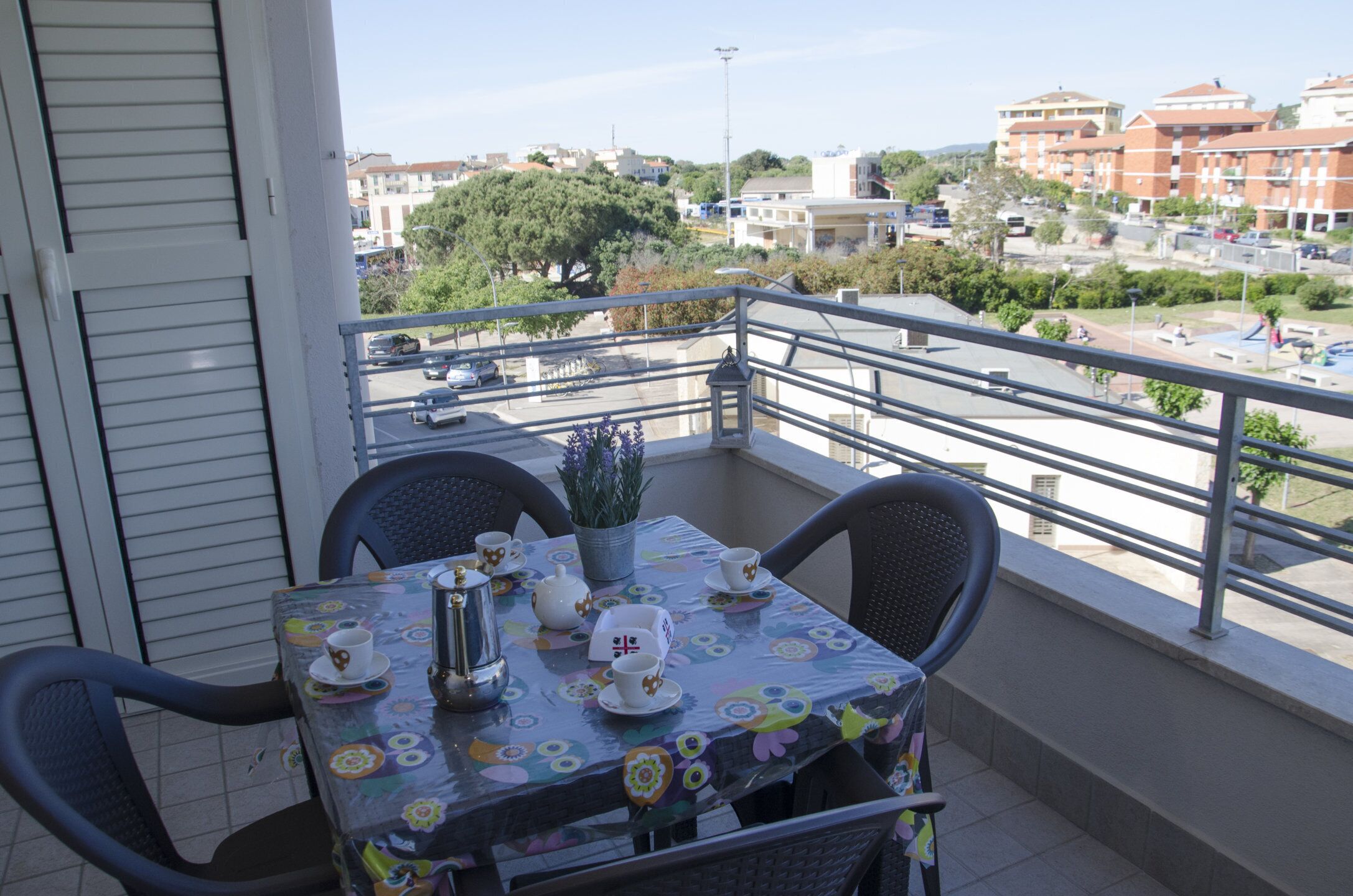 A balcony with a table set for tea, chairs, and a view of the cityscape.