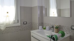 Ett badrum med ett vitt handfat, en spegel och ett fönster med en vit gardin.