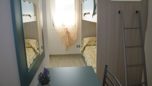 Ett rum med en våningssäng, ett skrivbord, en stol, en stege och ett fönster med gardiner.