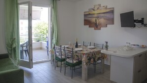 A dining area with a table set for four, a small kitchen counter, and a balcony with a chair. - Casa Tracina (Alghero)