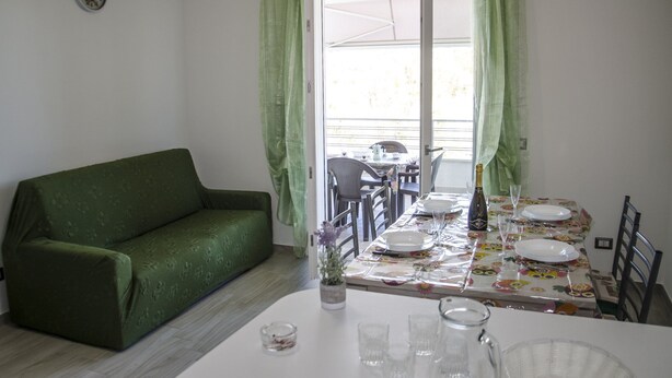 A dining area with a table set for two, a green sofa, and a clock on the wall. - Casa Tracina (Alghero)