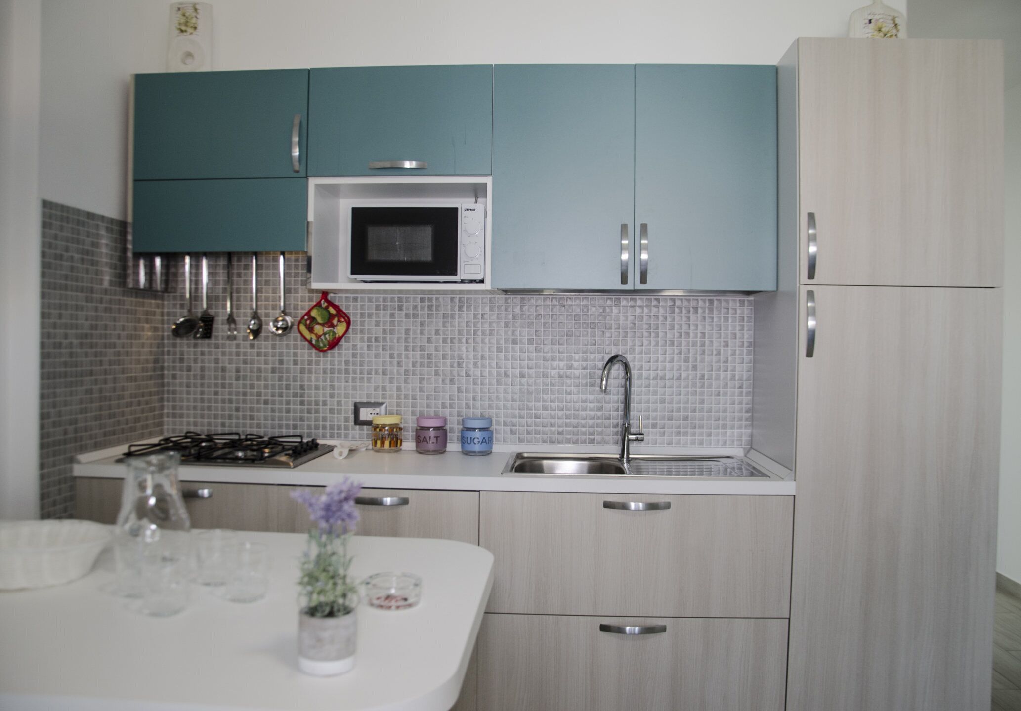 A kitchen with teal cabinets, a microwave, a sink, and a gas stove.