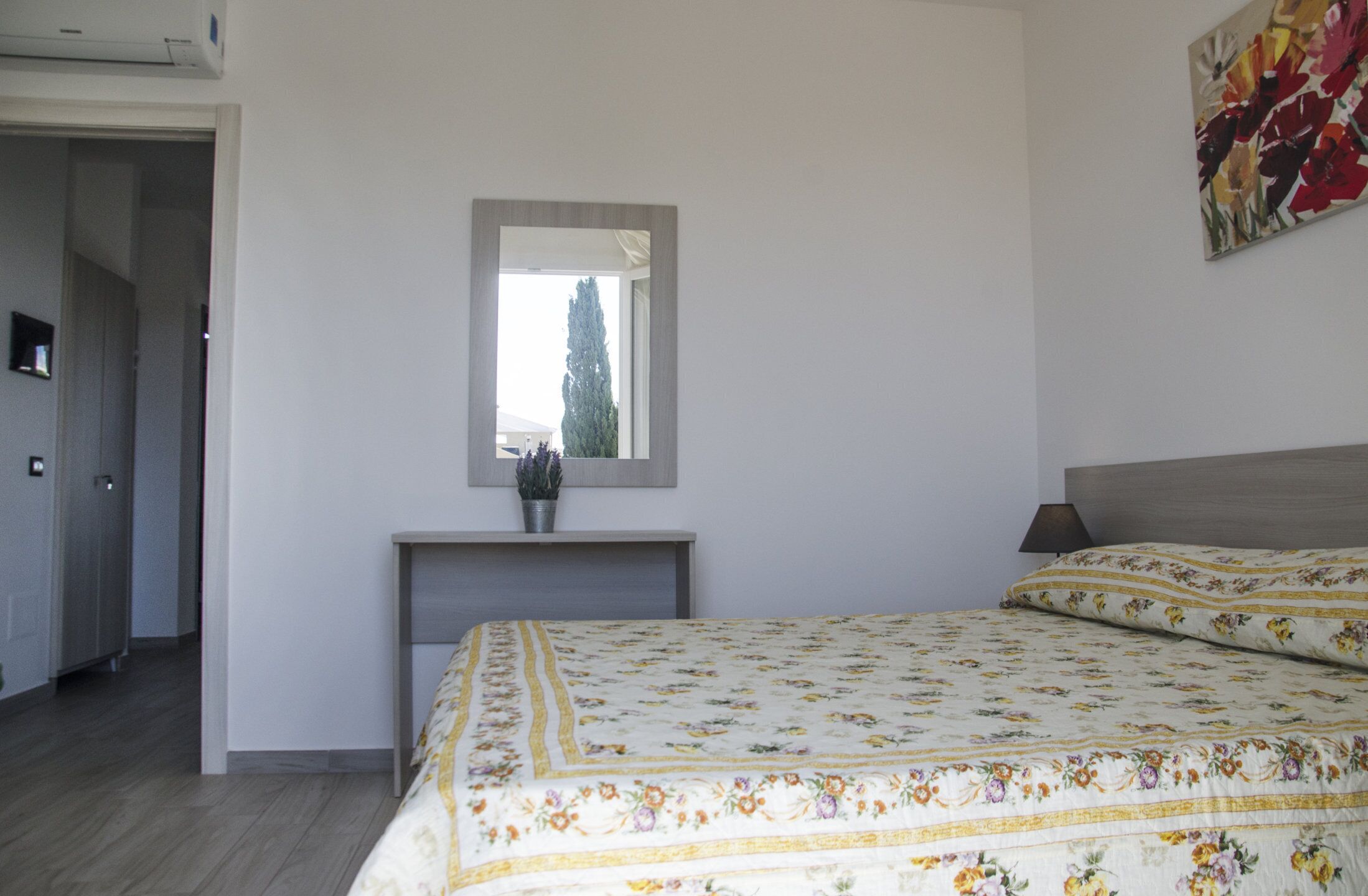 A bedroom with a bed, a bedside table, a mirror, and a potted plant.