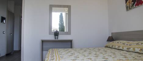 A bedroom with a bed, a bedside table, a mirror, and a potted plant.