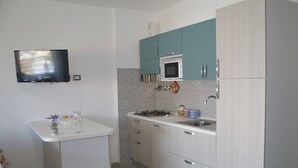 A modern kitchen with a flat-screen TV, a white countertop, teal cabinets, a microwave, and a gas stove. - Casa Tracina (Alghero)