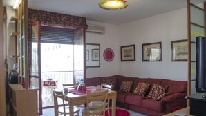 A living room with a red sofa, a wooden dining table with chairs, a TV, and framed pictures on the wall. - Casa Muggine (Alghero)