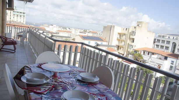 A balcony with a table set for dining, overlooking a cityscape. - Casa Muggine (Alghero)