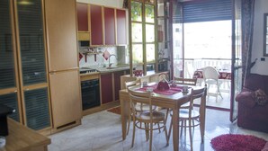 A modern kitchen with wooden cabinets, a dining table with chairs, and a balcony with a view. - Casa Muggine (Alghero)