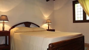 Quarto com cama de madeira, duas mesas de cabeceira com abajures, uma janela com cortinas e parede texturizada.