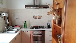 Uma cozinha compacta com coifa de aço inoxidável, forno embutido e máquina de lavar.