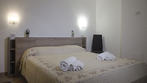 A hotel room with a bed, two bedside lamps, a nightstand, a chair, and a small table with a plant. - Casa Valverde (Alghero)