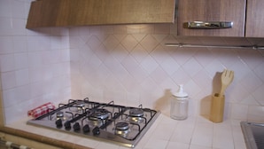 A kitchen with a gas stove, a wooden cabinet above, and a tiled backsplash. - Casa Valverde (Alghero)
