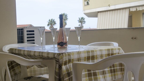 A table with a bottle of Akenta wine and four glasses on a balcony with a view of palm trees and buildings.