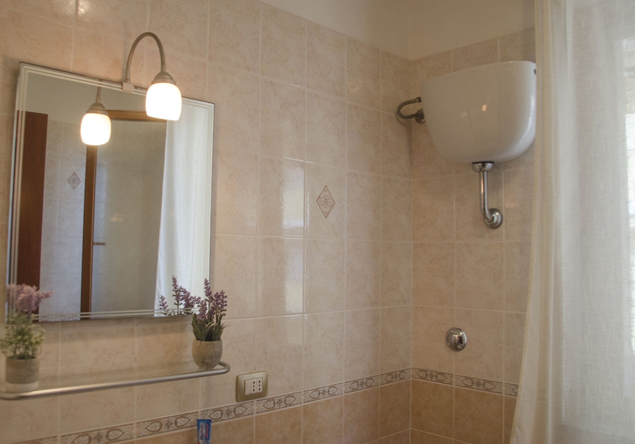 Une salle de bain avec un lavabo fixé au mur, un miroir avec éclairage intégré et une plante en pot posée sur le comptoir.