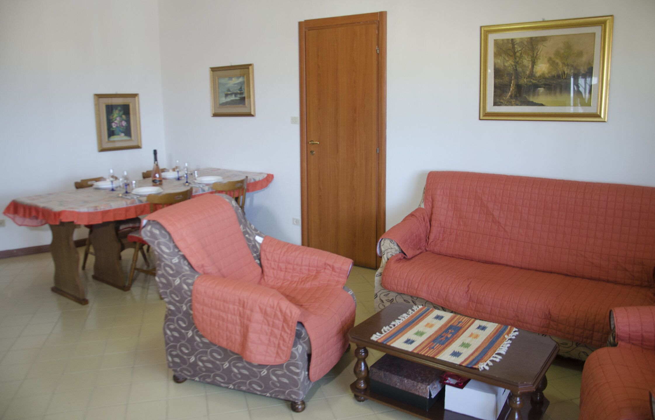 A living room with a sofa, armchair, coffee table, and dining table set with plates and candles.