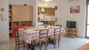 A dining area with a table set for four, surrounded by wooden chairs. A kitchen is visible in the background with wooden cabinets and a stove. - Casa Lampuga (Alghero)