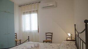 A bedroom with a bed, two chairs, a wardrobe, and an air conditioning unit. - Casa Lampuga (Alghero)