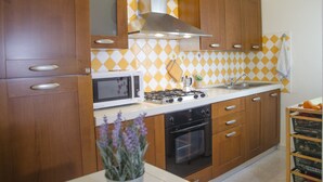 A kitchen with wooden cabinets, a microwave, a stove, and a sink. - Casa Lampuga (Alghero)