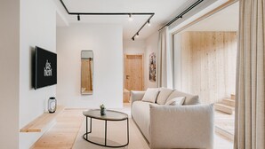 A modern living room with a sofa, a coffee table, a TV mounted on the wall, and a large window with curtains. - das bleibt (Schladming)