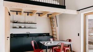 A compact kitchen with a dining area, a loft bedroom with a balcony, and a visible staircase. - das bleibt (Schladming)