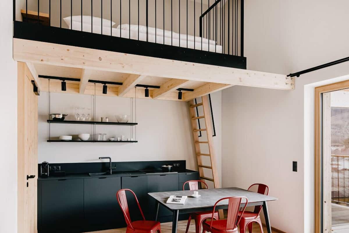 A compact kitchen with a dining area, a loft bedroom with a balcony, and a visible staircase.