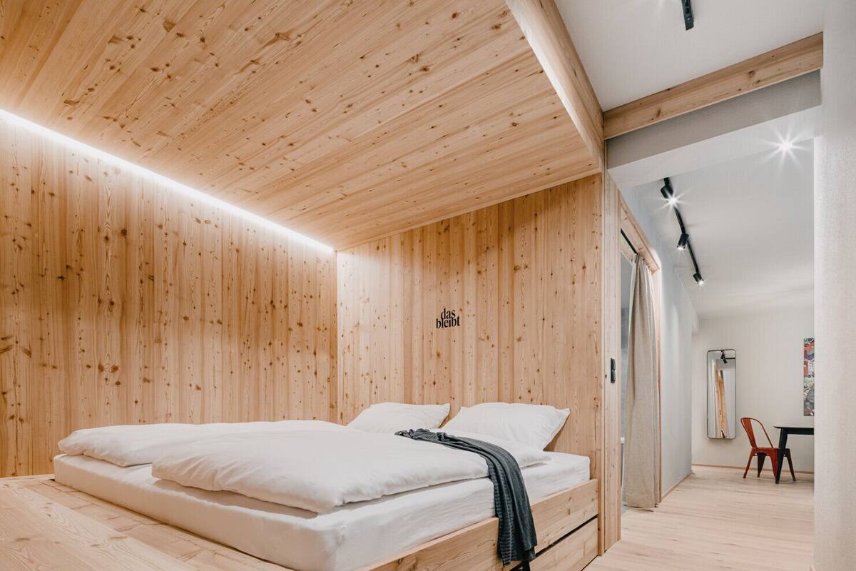 A modern bedroom with a wooden ceiling, a bed with white bedding, and a small desk area.