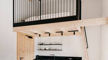 A compact kitchen with a dining area, featuring a wooden ceiling, black railings, and red chairs.