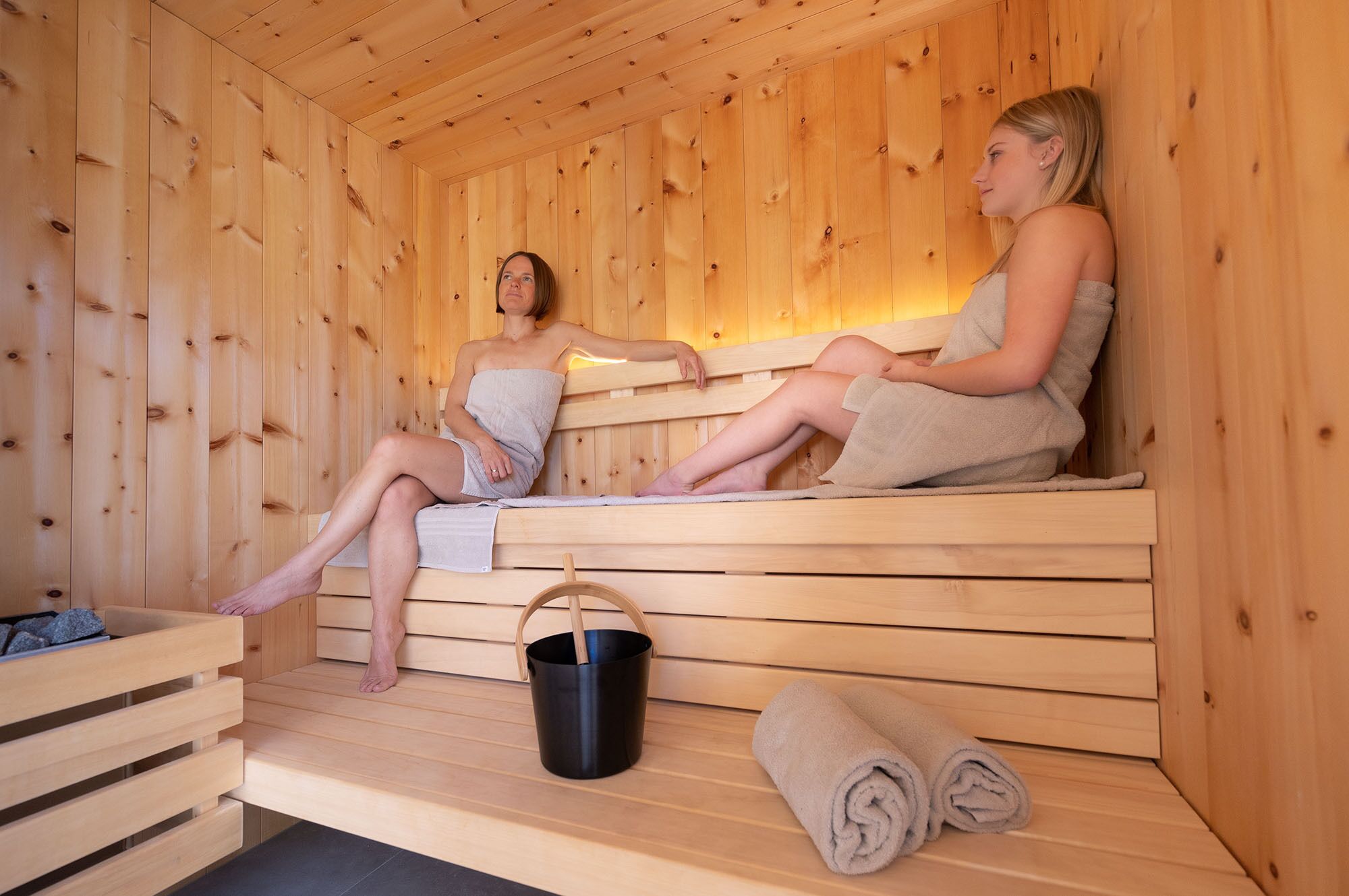 Un sauna en bois avec deux bancs, un seau noir et des serviettes enroulées.