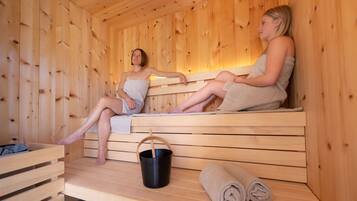 Un sauna en bois avec deux bancs, un seau noir et des serviettes enroulées.
