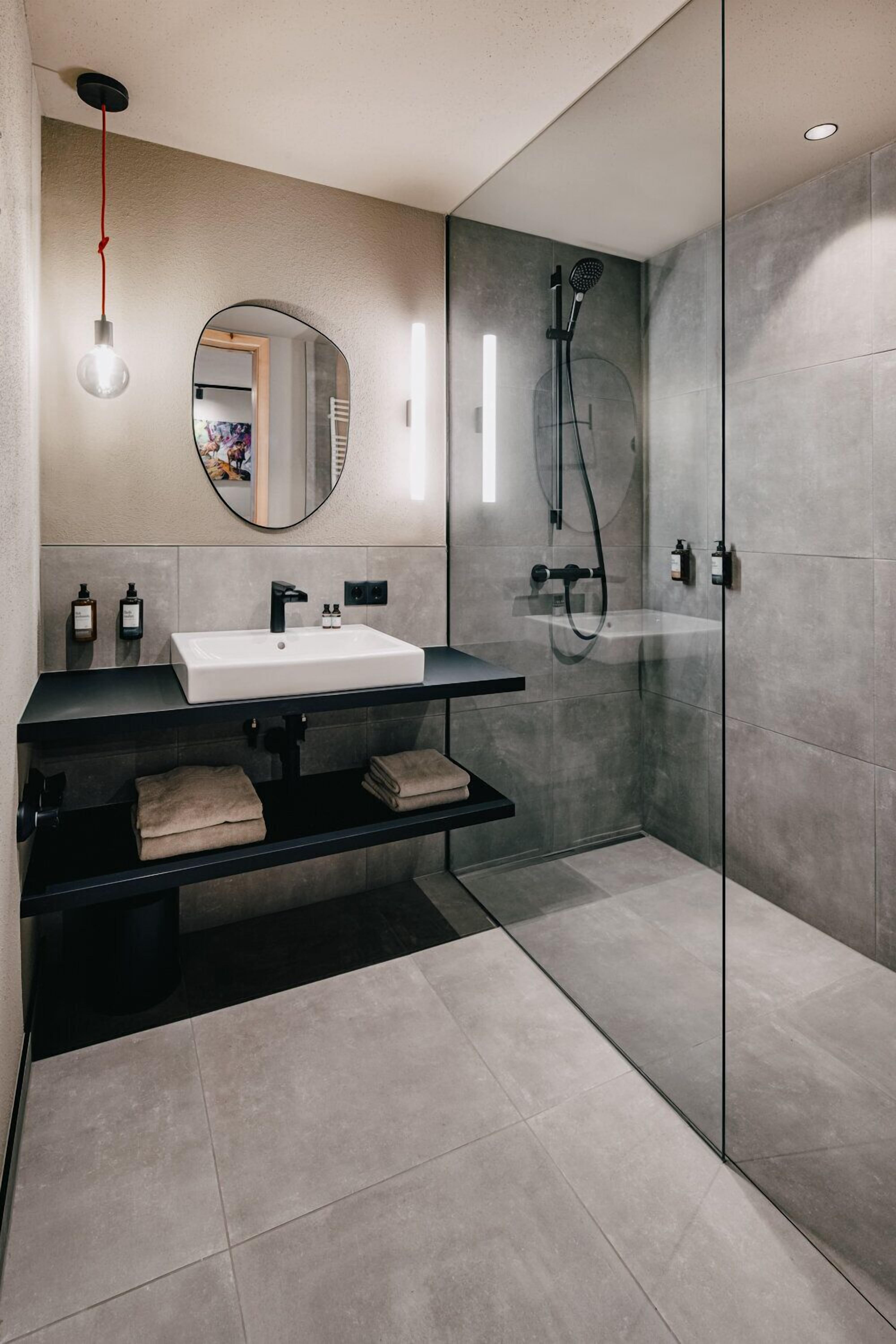 Un bagno moderno con doccia vetrata, lavandino bianco e piano di appoggio nero.