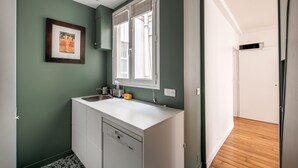A kitchen with a white countertop, a sink, and a window with blinds. - Spacious flat in Batignolles quarter (Paris)