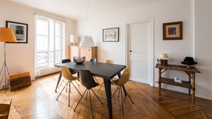 A dining area with a dark table, four chairs, a bowl, and a lamp. There's a wooden cabinet, a door, and a small table with hats. - Spacious flat in Batignolles quarter (Paris)