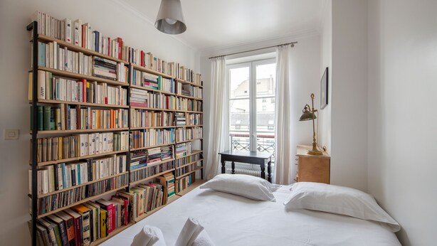 A bedroom with a large bookshelf, a bed with white linens, and a window with curtains. - Spacious flat in Batignolles quarter (Paris)