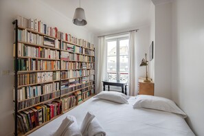 A bedroom with a large bookshelf, a bed with white linens, and a window with curtains. - Spacious flat in Batignolles quarter (Paris)