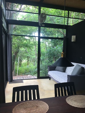 Une pièce avec une grande fenêtre, un ventilateur, un canapé et une table à manger.